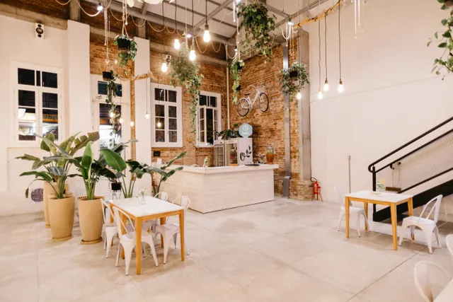 Bright cafe dining area with wooden tables, chairs, a service counter, and potted plants.