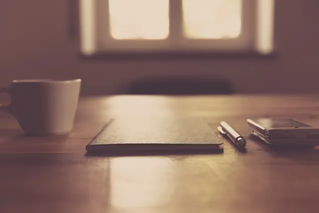Cup, notebook, pen, and phone arranged on a wooden desk.