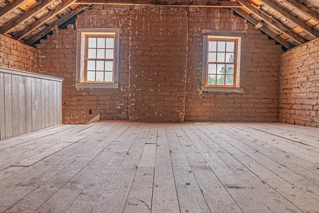 Unfinished attic interior with exposed roof framing and brick walls.