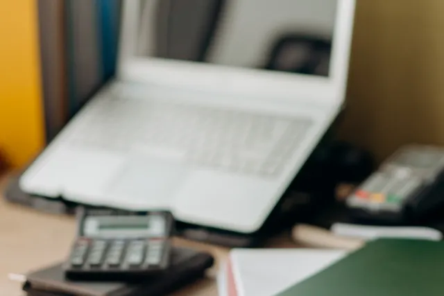 Laptop and folders on a desk beside a calculator.